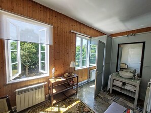 A wooden-paneled room with a large window, a radiator, a table with a lamp, and a bathroom with a sink and mirror. - Pizarra by Interhome (Vilalba)