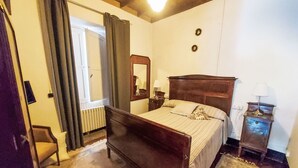 Un dormitori amb un llit de fusta, una tauleta de nit, un mirall i una finestra amb cortines.