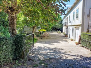 Ein gepflasterter Innenhof mit Tisch und Stühlen, umgeben von Gebäuden und Grünflächen.