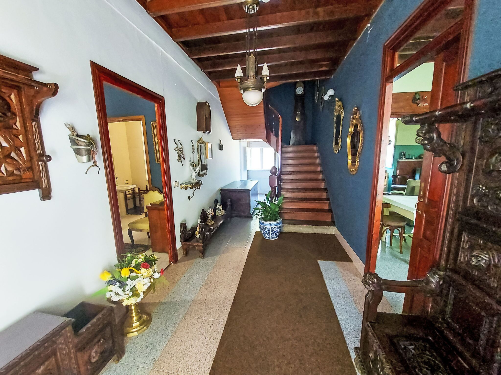 Un couloir avec un escalier, des portes en bois et divers objets fixés aux murs.
