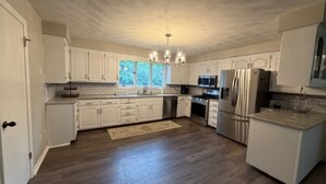 A kitchen with white cabinets, a central island, stainless steel appliances, and a chandelier. - The Massillon Retreat! (Massillon)