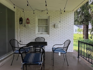 Eine überdachte Terrasse mit einer Ziegelwand, einem Tisch mit Stühlen, Lichterketten und einem Fenster.