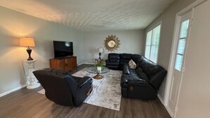 A living room with a sectional sofa, a coffee table, a television, and a decorative mirror. - The Massillon Retreat! (Massillon)