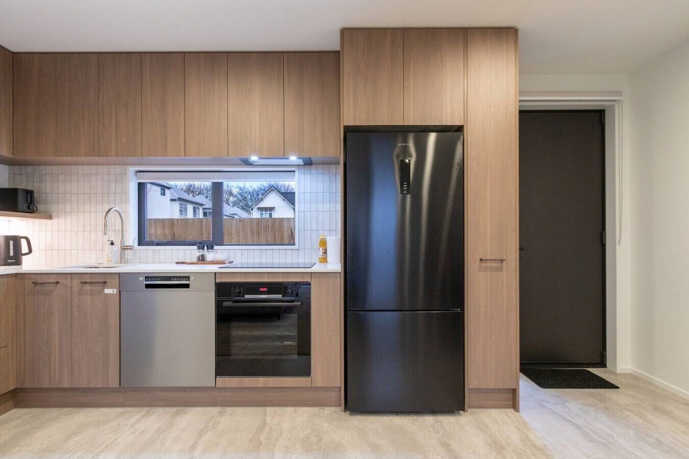 A modern kitchen with wooden cabinets, a stainless steel refrigerator, a dishwasher, and an oven.