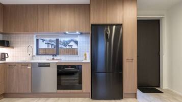 A modern kitchen with wooden cabinets, a stainless steel refrigerator, a dishwasher, and an oven.