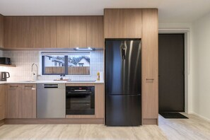A modern kitchen with wooden cabinets, a stainless steel refrigerator, a dishwasher, and an oven.