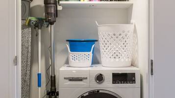 A laundry room with a Bosch washing machine, a drying rack, and a shelf with various items.