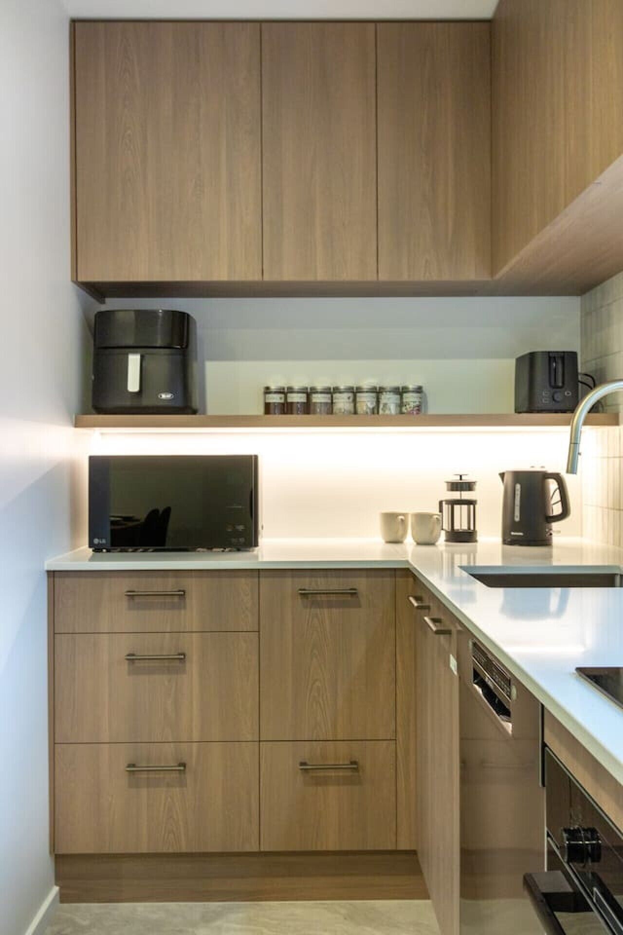A modern kitchen with wooden cabinets, a built-in microwave, and a coffee maker.