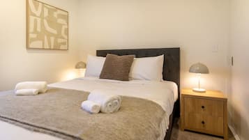 A neatly made bed with white linens, a grey headboard, and two bedside lamps.