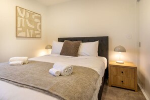 A neatly made bed with white linens, a grey headboard, and two bedside lamps.