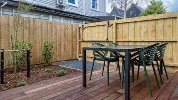 A wooden deck with a table and chairs, surrounded by a wooden fence and a small garden area.