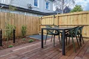 A wooden deck with a table and chairs, surrounded by a wooden fence and a small garden area.