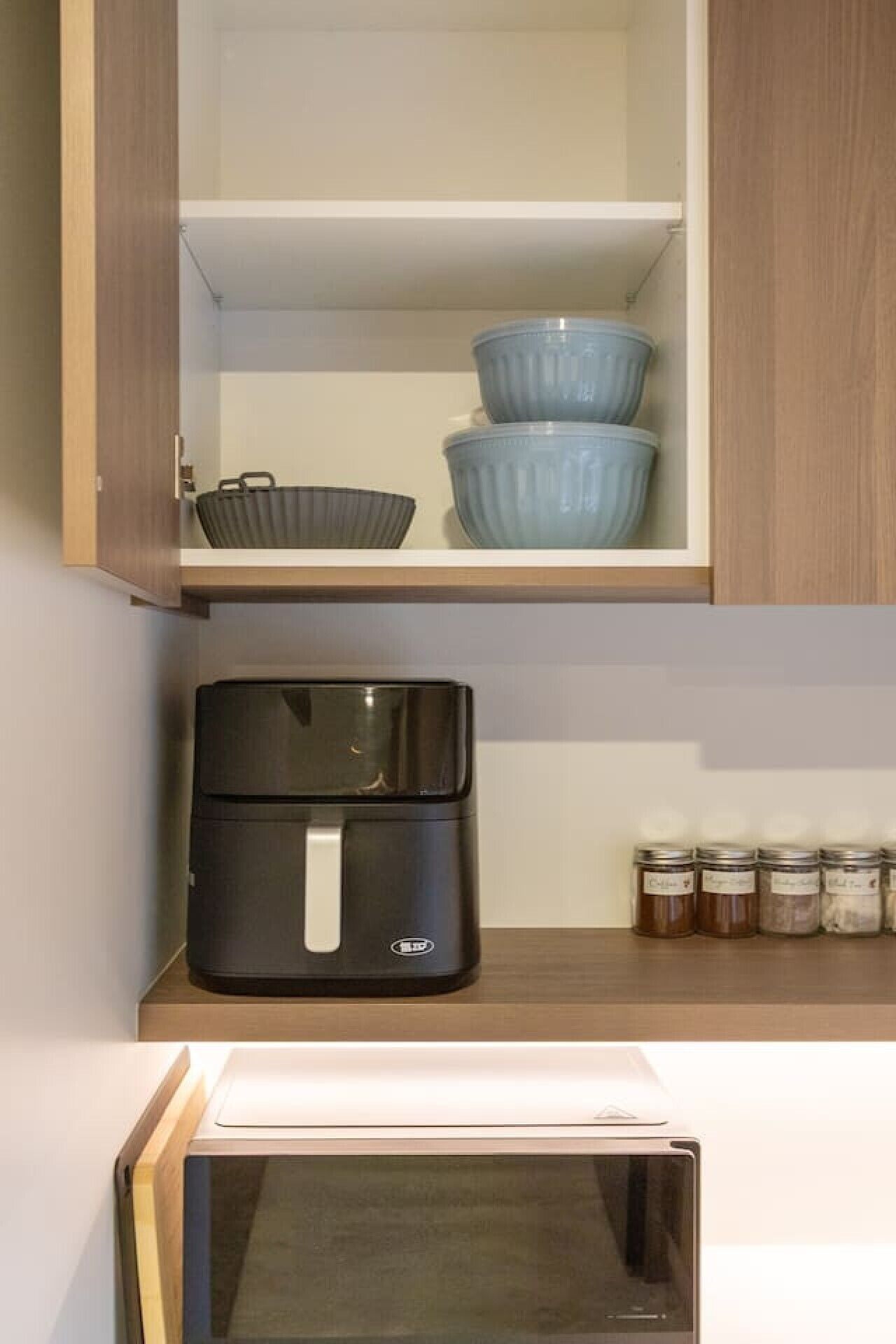 A kitchen with a microwave, a black appliance on the counter, and jars on the shelf.