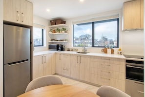 Eine moderne Küche mit hellen Holzschränken, einem Edelstahlkühlschrank und einem großen Fenster mit Blick ins Freie.