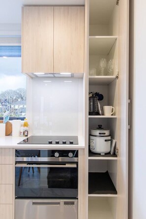 A compact kitchen with a built-in oven, a stovetop, and a microwave. There is a window providing a view of the outside. - Walk Everywhere! CBD Pad + Stadium & Parking (Christchurch)
