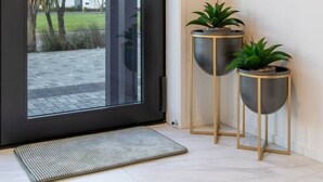 Una entrada moderna con puerta corredera de vidrio, un felpudo y dos plantas en macetas sobre mesitas.