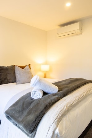 Ein Hotelzimmer mit einem Bett, Kissen, einer Decke, einer Lampe und einer Klimaanlage.