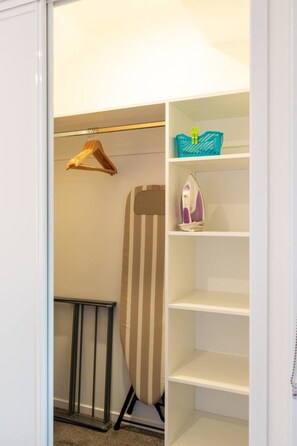 Ein begehbarer Kleiderschrank mit Kleiderstange, Regalen und einem gestreiften Bügelbrett.