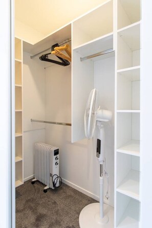 Ein begehbarer Kleiderschrank mit offenen Regalen, einem Heizkörper und einem Standventilator.
