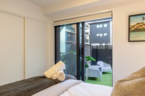 Une chambre d’hôtel avec un lit, une fenêtre et une vue sur un balcon agrémenté de chaises et sur un immeuble.