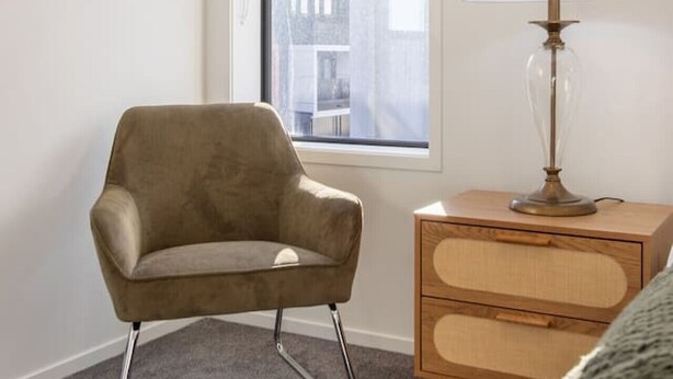 Una habitación con ventana, una silla, una lámpara y un aparador.