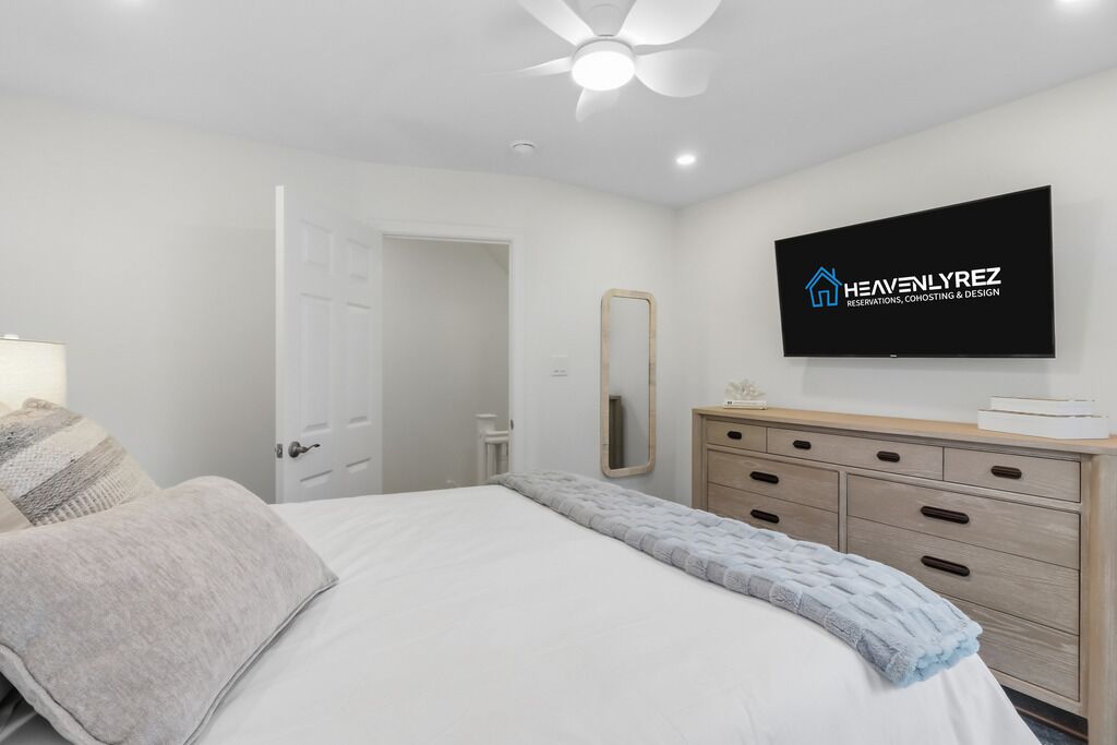 Une chambre à coucher comprenant un lit, une commode, un miroir, un téléviseur et un ventilateur de plafond.