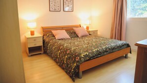 Quarto com cama de madeira, duas mesas de cabeceira com luminárias, um criado-mudo e uma janela com cortinas.