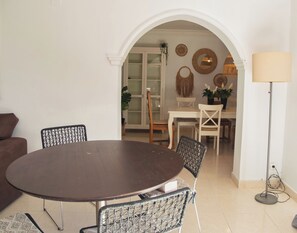 Un comedor con una mesa redonda, sillas, una lámpara y una puerta que da a una cocina.