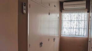 Quarto com guarda-roupa, janela com cortina e uma pequena cesta no chão.