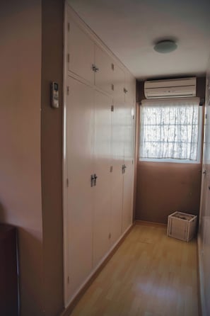 A room with a wardrobe, a window with a curtain, and a small basket on the floor.