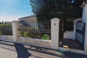 A gated property with a paved entrance, a metal fence, and a building with a tiled roof.