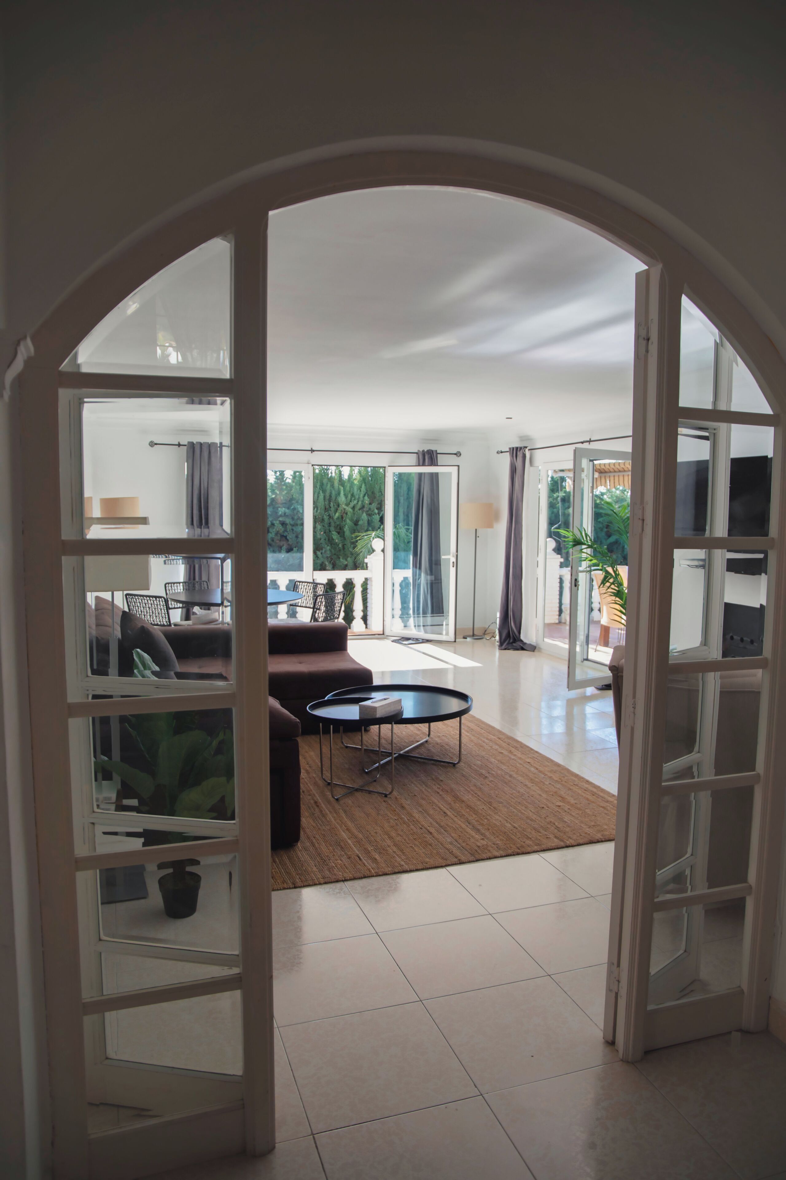 An open archway leading to a living area with a sofa, a coffee table, and a view of a balcony with plants.