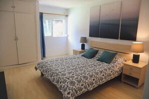A bedroom with a bed, a wardrobe, a nightstand, a lamp, and a window with curtains.