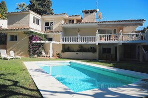 Ein zweistöckiges Haus mit Swimmingpool, einem Balkon mit weißen Geländern und einem Garten mit Gartenmöbeln.