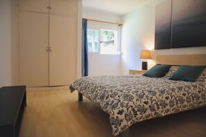 Ein Schlafzimmer mit einem Bett, einem Kleiderschrank, einem Nachttisch mit Lampe und einem Fenster mit Vorhängen.
