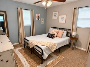 A bedroom with a bed, a ceiling fan, a bedside table, a lamp, and a window with curtains. - Dog Lovers' Dream  Wash Station + Dog Library (Warner Robins)