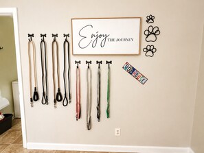 A wall with multiple dog leashes hanging on hooks, a framed inspirational quote, a decorative wall plaque, and a small license plate. - Dog Lovers' Dream  Wash Station + Dog Library (Warner Robins)