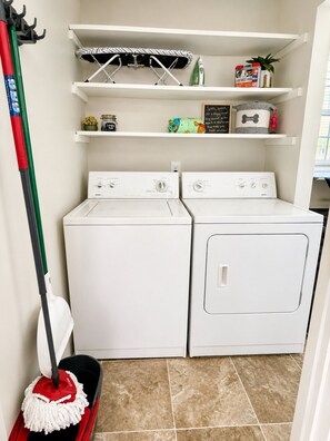 A laundry area with two white washing machines, a mop, and a shelf with various items including a plant and a container labeled 'fetch'. - Dog Lovers' Dream  Wash Station + Dog Library (Warner Robins)