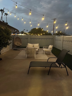 Eine Terrasse im Freien mit Lichterketten, einem Hängesessel und einer Liege.