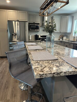 A modern kitchen with a granite countertop, stainless steel appliances, and a seating area with mesh chairs. - Tempe Luxury Oasis 10 mins from ASU, Old Town and PHX (Tempe)