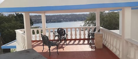 Un espace extérieur abrité, doté d’un sol rouge, d’une rambarde blanche et de chaises en métal.