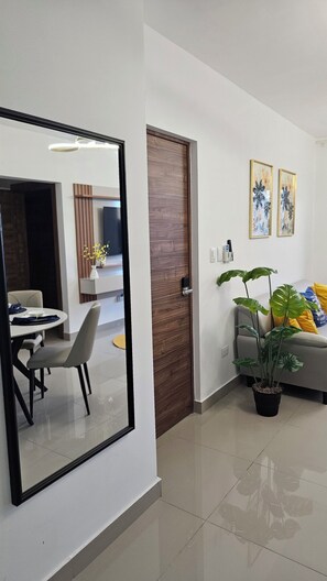 Una sala moderna con comedor, un espejo grande, una puerta de madera y una planta en maceta.