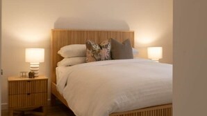 Ein Schlafzimmer mit einem hölzernen Bett, zwei Nachttischen mit Lampen sowie einer Hängeleuchte.