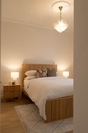 Ein Schlafzimmer mit einem hölzernen Bett, zwei Nachttischen mit Lampen sowie einer Hängeleuchte.