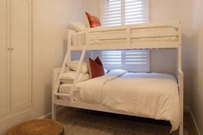A bunk bed with a ladder, white bedding, and a window with blinds.