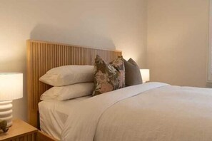 Un lit bien fait, avec une tête de lit en bois, deux lampes de chevet et un coussin à motifs floraux.