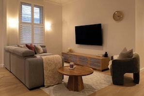 A modern living room with a sofa, a coffee table, a television, and a clock on the wall.