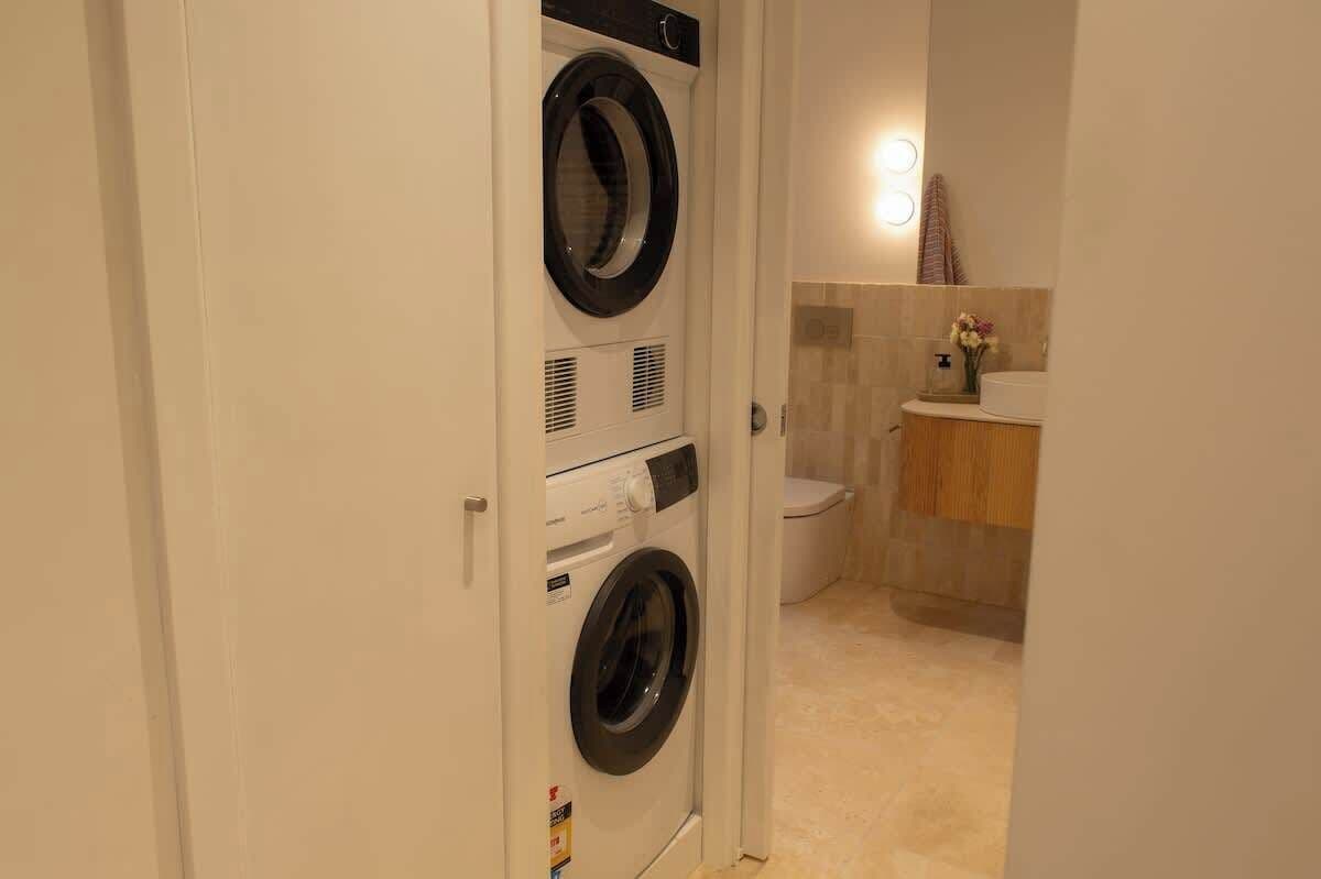 A laundry room with a front-loading washer and dryer, a toilet, and a sink with a mirror.