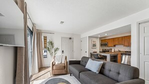 A modern living room with a grey sofa, a small round coffee table, and a beige armchair. - Extended Stay Fully Furnished Studios At The Cass (Omaha)