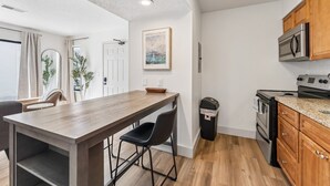 A modern kitchen with wooden cabinets, a stainless steel oven, and a dining area with a wooden table and chairs. - Extended Stay Fully Furnished Studios At The Cass (Omaha)